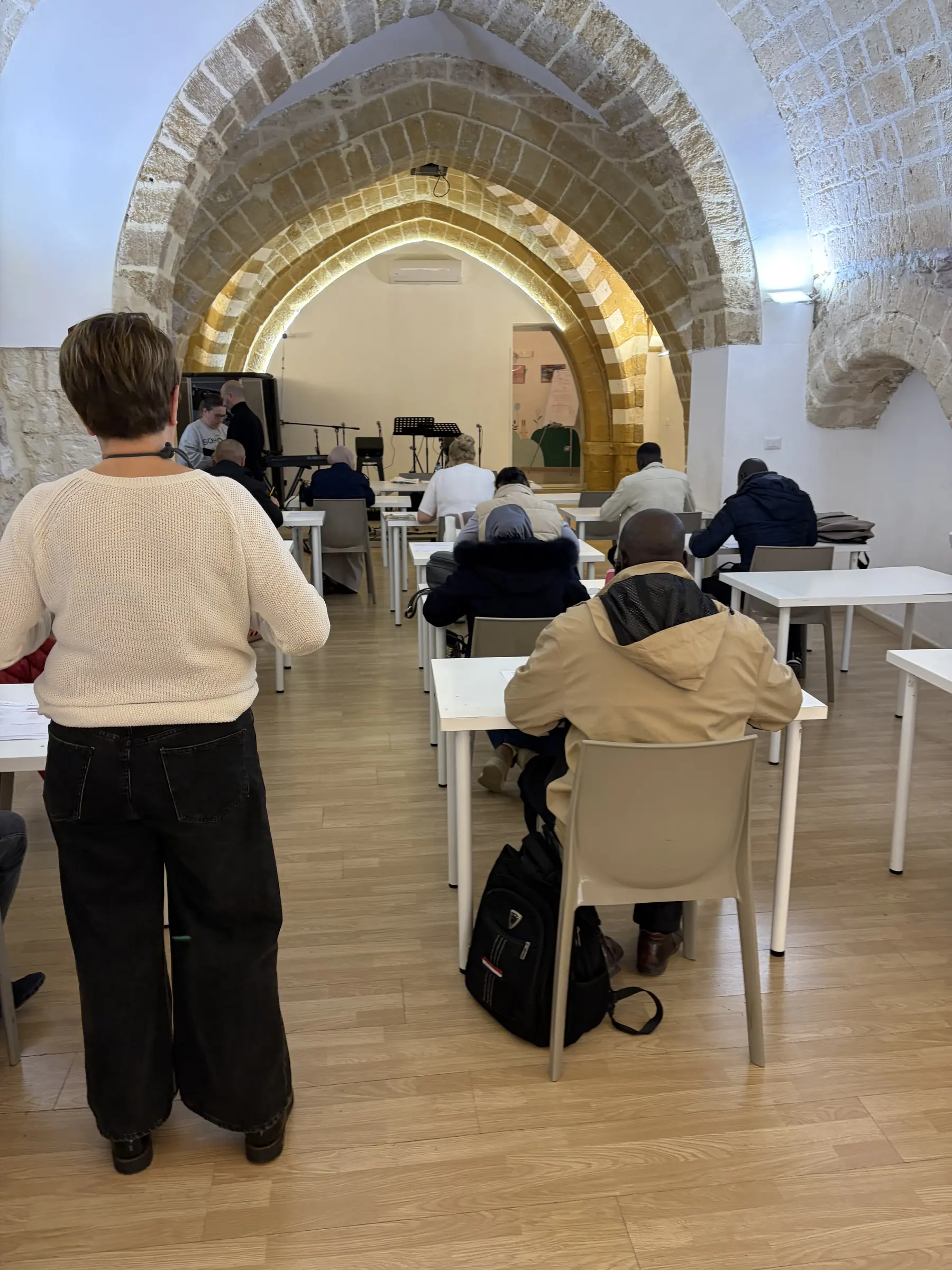 Un'insegnante segue una lezione di italiano: adulti al lavoro sui banchi, sotto gli archi in pietra della sede