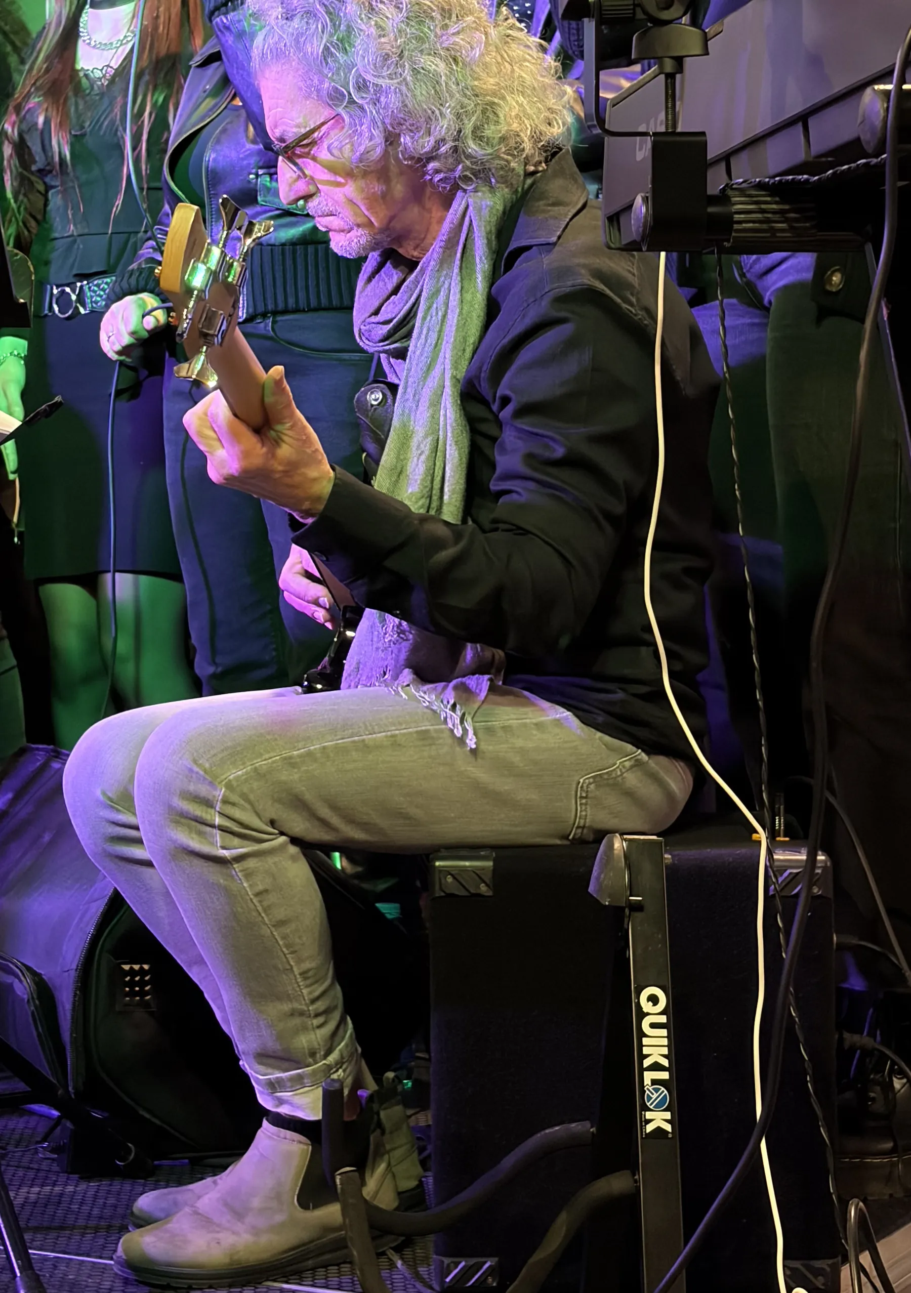 An adult bass player plays seated on stage during a concert