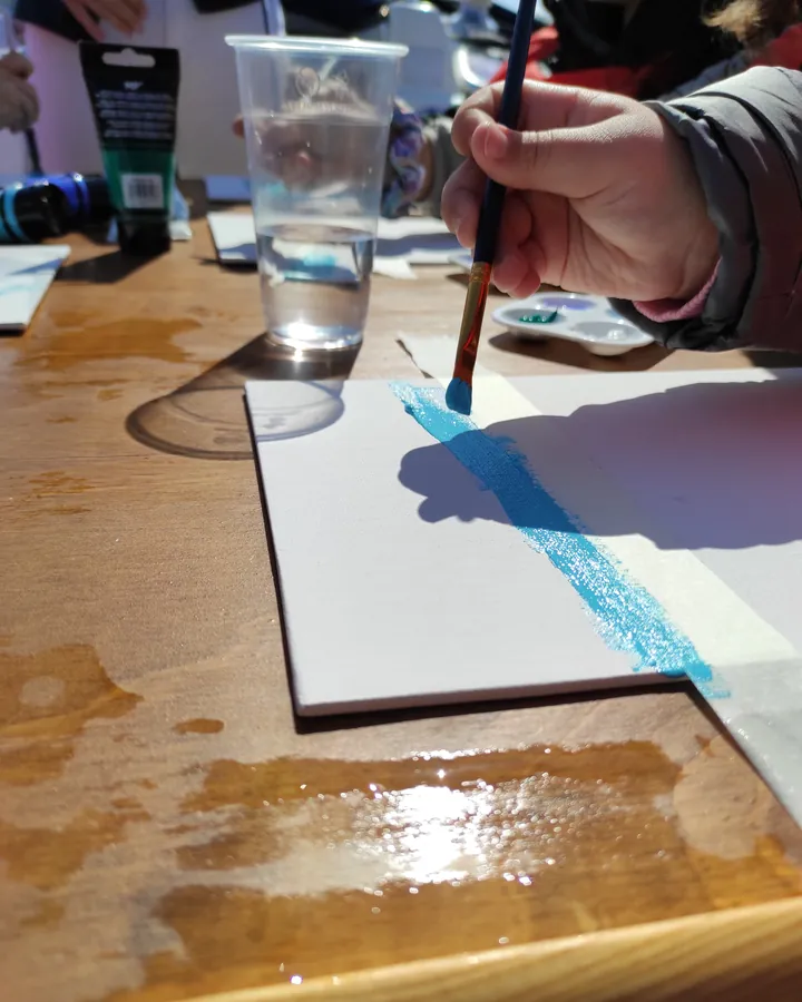 Una mano stende l'azzurro con il pennello su un foglio durante il laboratorio di pittura