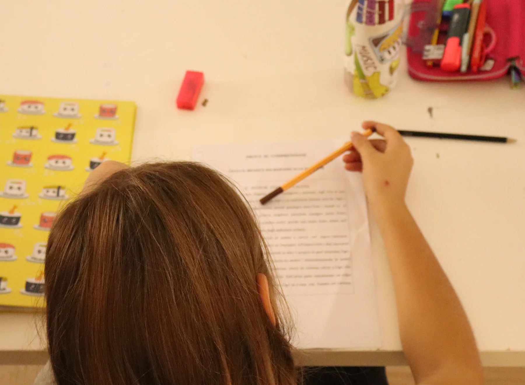 Una ragazza, ripresa di spalle, legge un foglio con la matita in mano al tavolo di studio