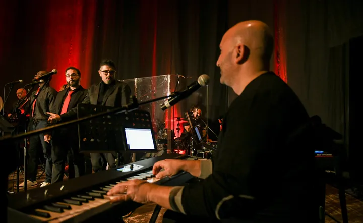 Musicians and singers on stage together: keyboard up front, vocals, guitar and drums