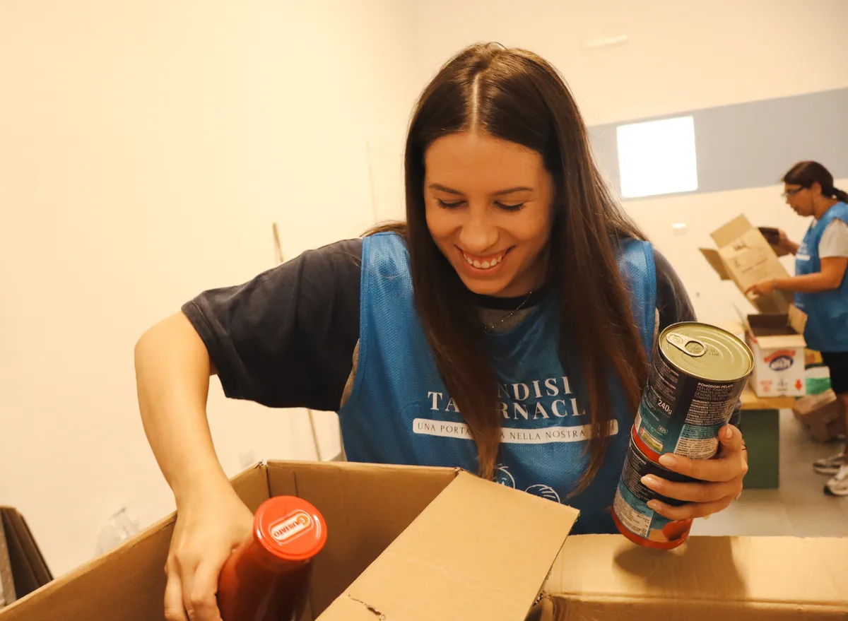 A volunteer smiles as she fills a box with food at the Dream Center