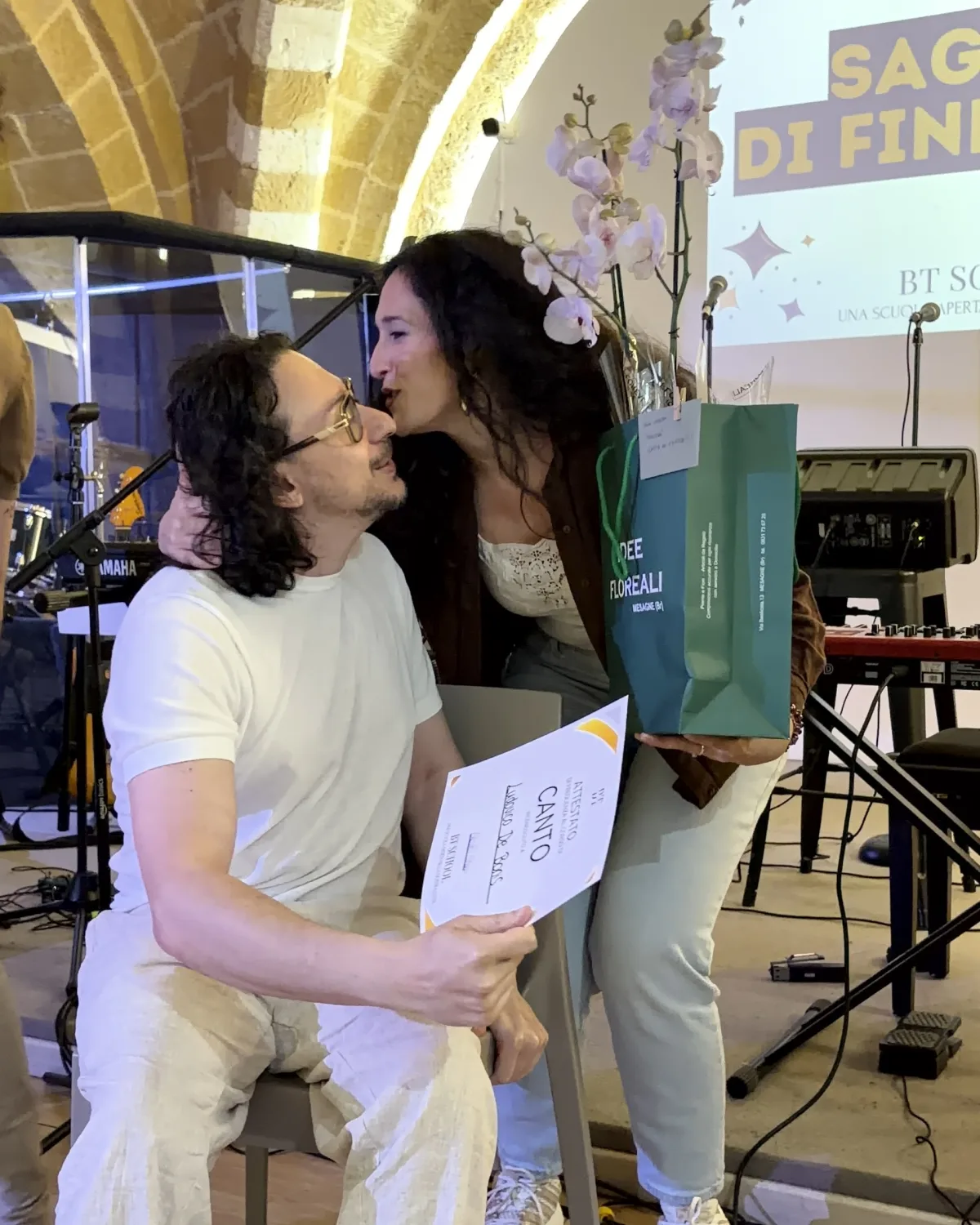 Miriam congratulates a student holding his singing course certificate at the end-of-year recital