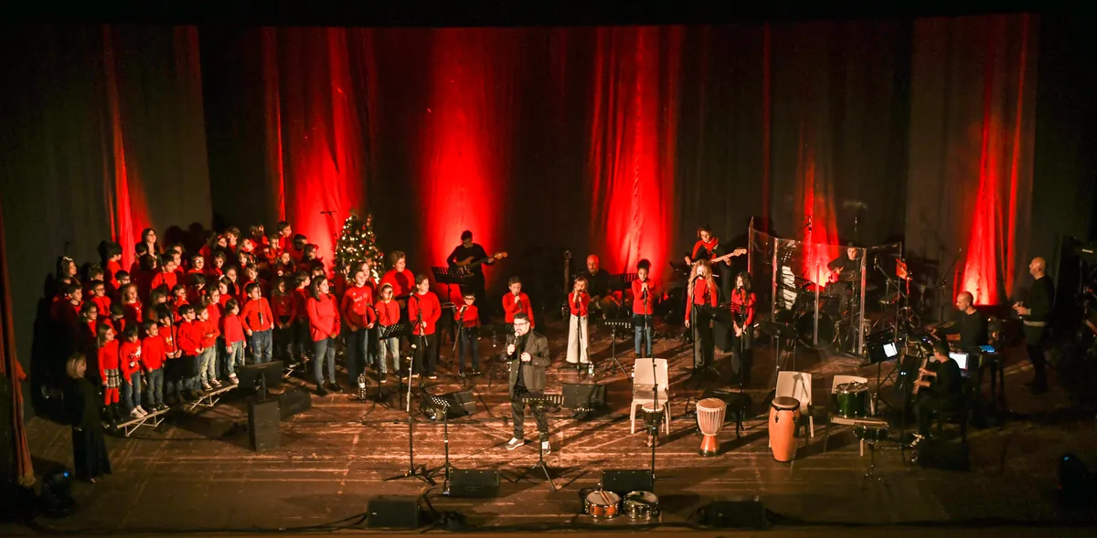 The full choir on the theatre stage at the Christmas concert, with the band under red lights