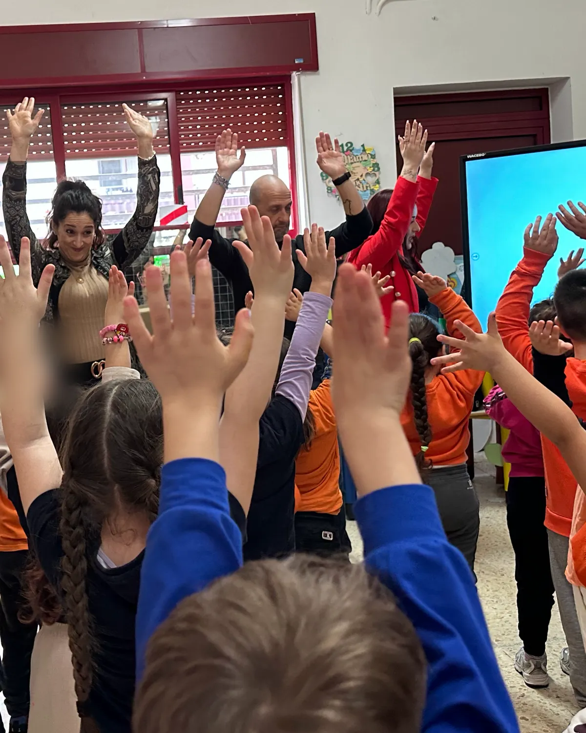Insegnanti e bambini cantano e ballano in inglese con le braccia alzate durante English Through Music