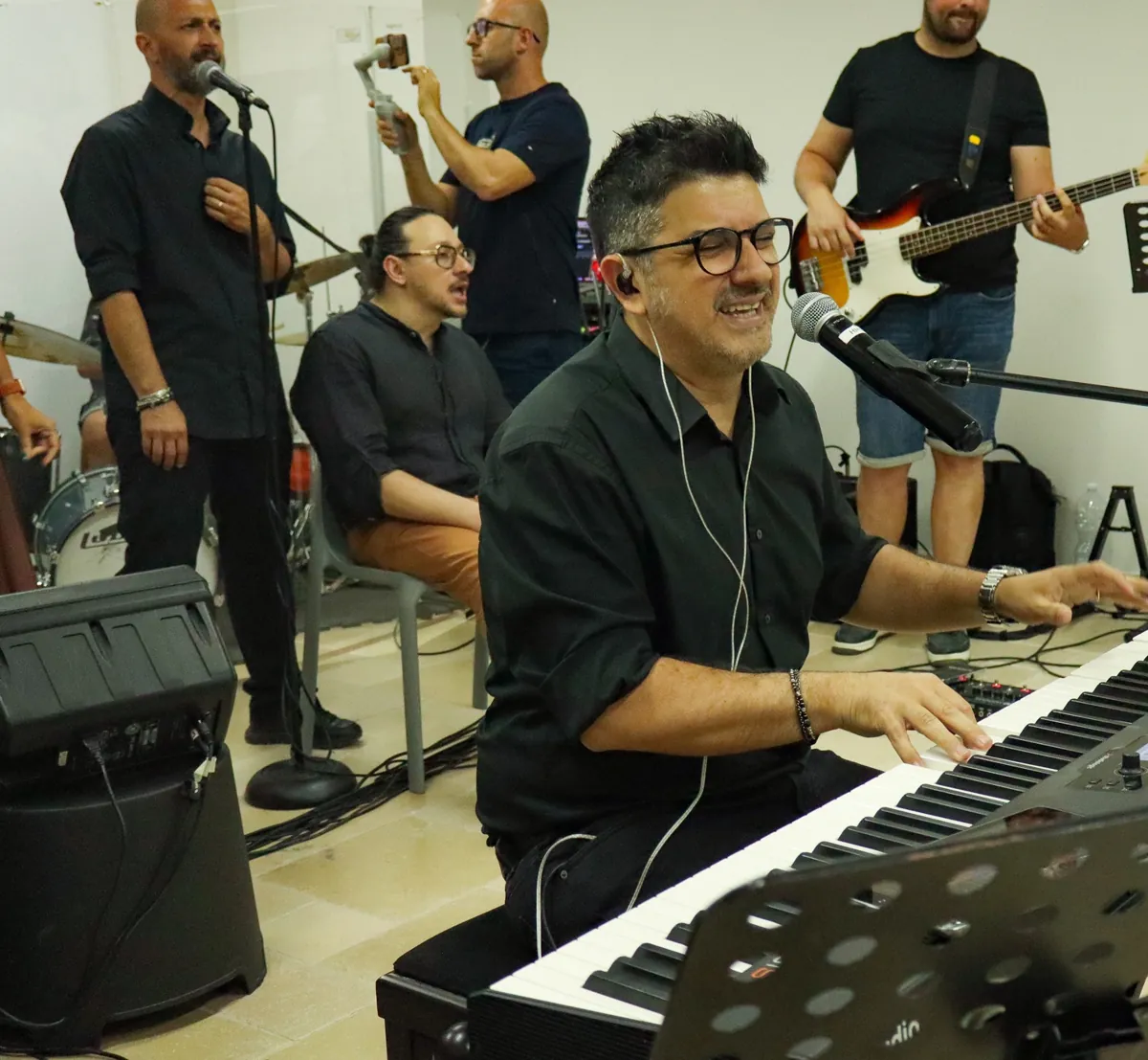A pianist sings into the microphone during a concert, with the band behind him