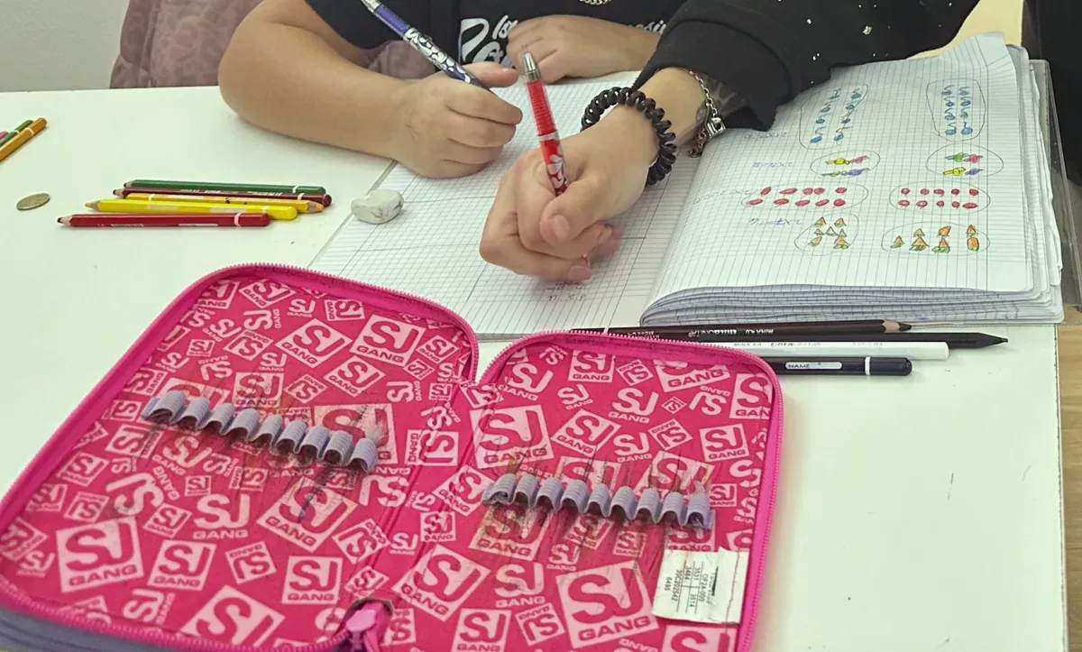Hands writing in a notebook during after-school tutoring, colored pencils on the desk