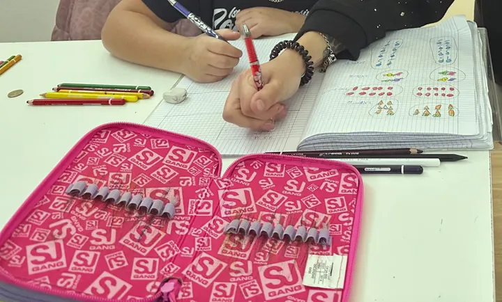 Mani che scrivono su un quaderno durante il doposcuola, con matite colorate sul banco